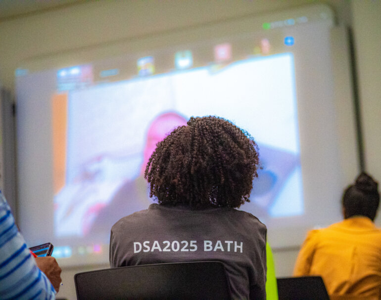 Sheila Ronoh looks on as an online participant presents. Volunteers ensure that online attendees get the best experience.
